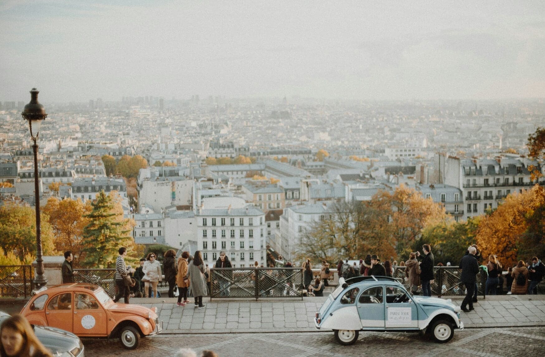 Romantic view over Paris. Two old cars and many people gaze at the city in bright, soft light.