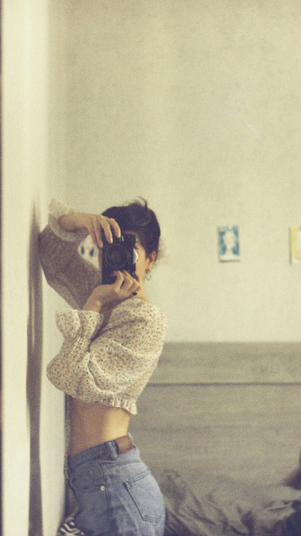 Una mujer está apoyada de frente contra la pared en una habitación luminosa y fotografía al espectador. La escena tiene un aire documental.