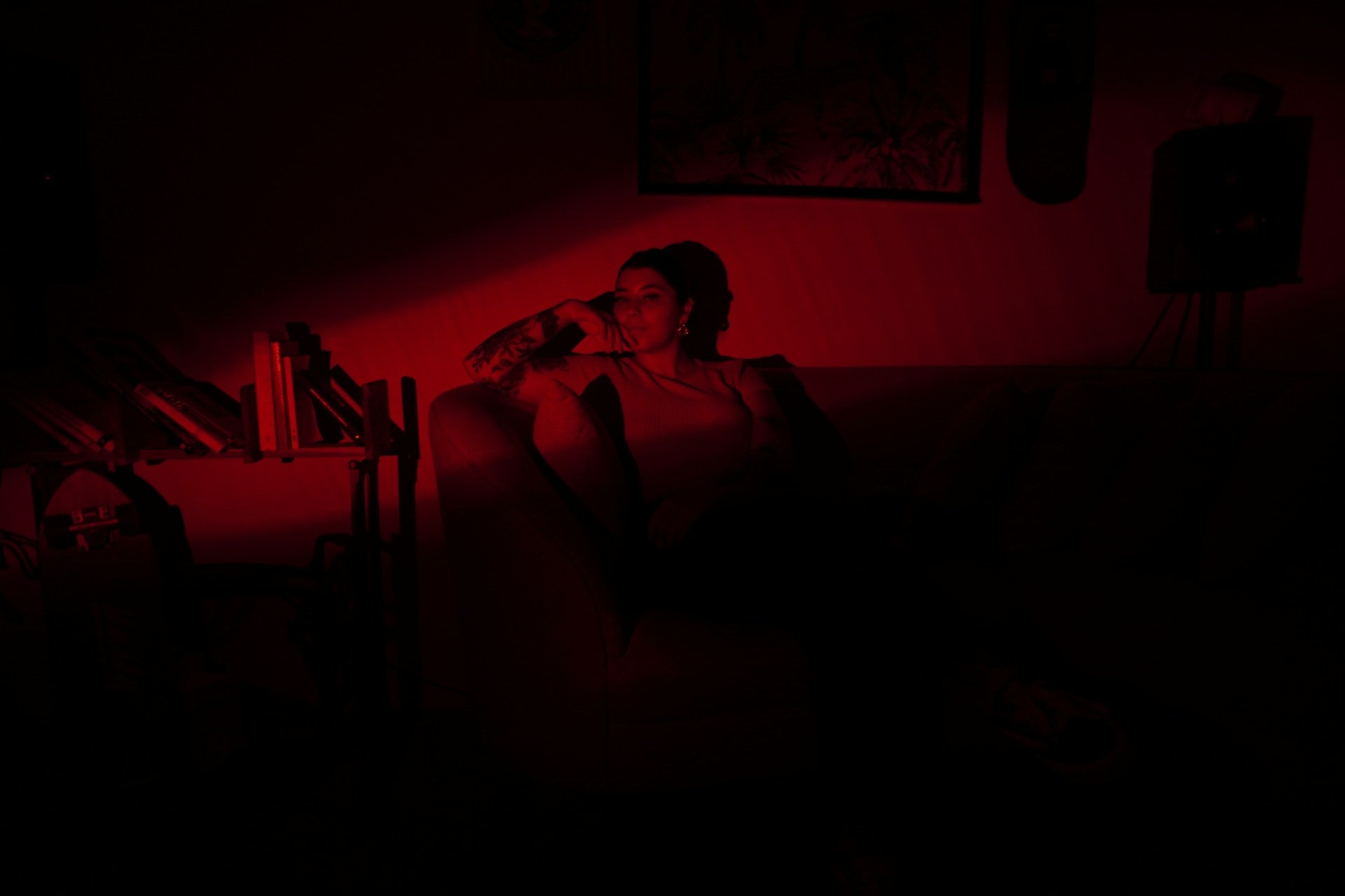 Una mujer tatuada está sentada en el sofá de una habitación oscura. Una luz roja la ilumina en la penumbra.