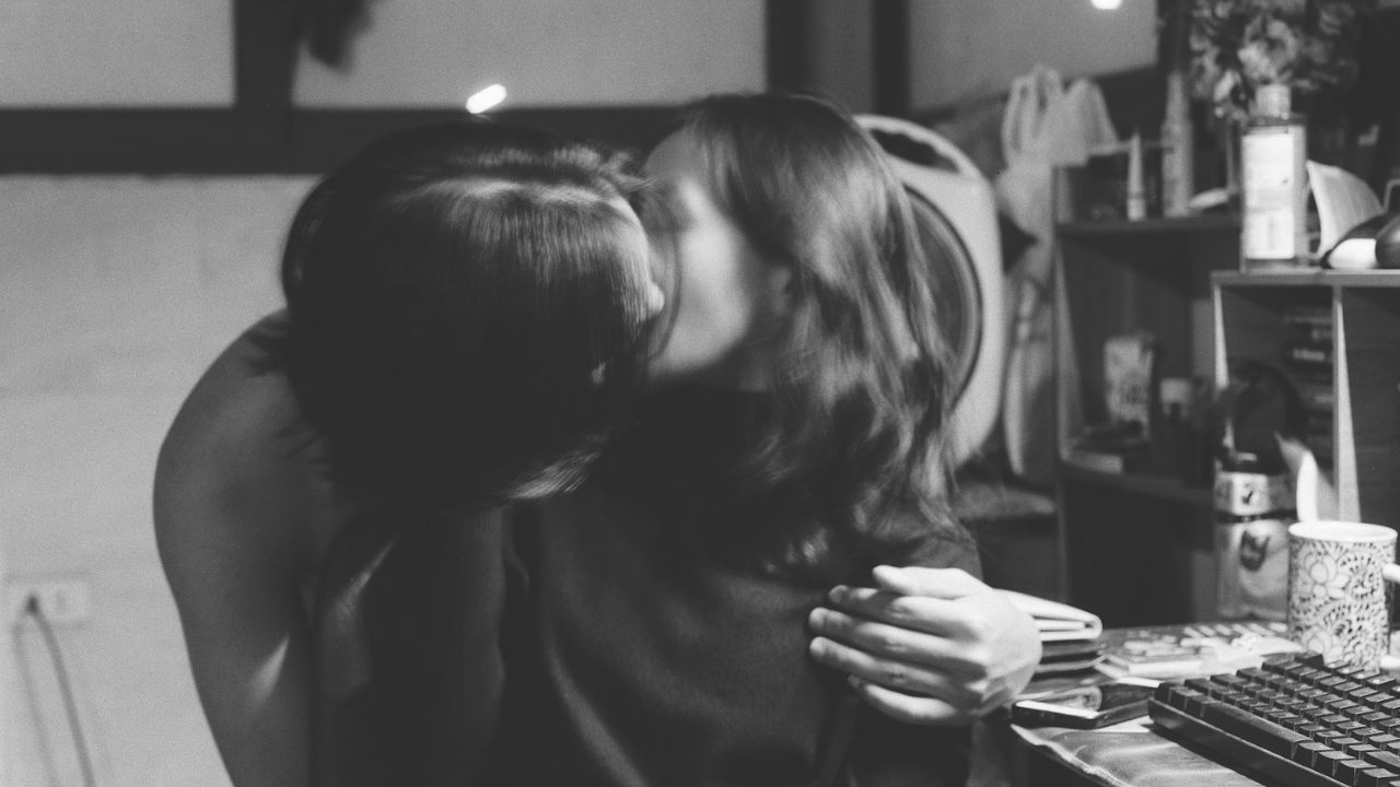 Woman is kissed from behind by a man in a black-and-white picture.