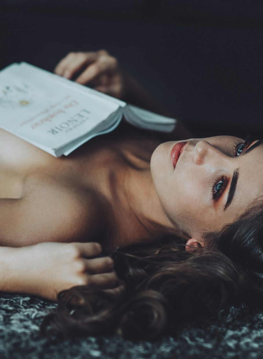 Mujer recostada tranquilamente en el suelo con un libro abierto sobre el pecho, mirada serena y reflexiva