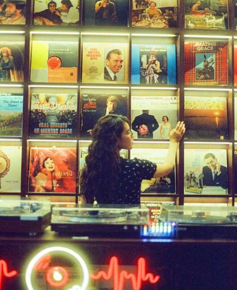 Frau betrachtet eine Wand mit Schallplatten in einem warm beleuchteten Raum