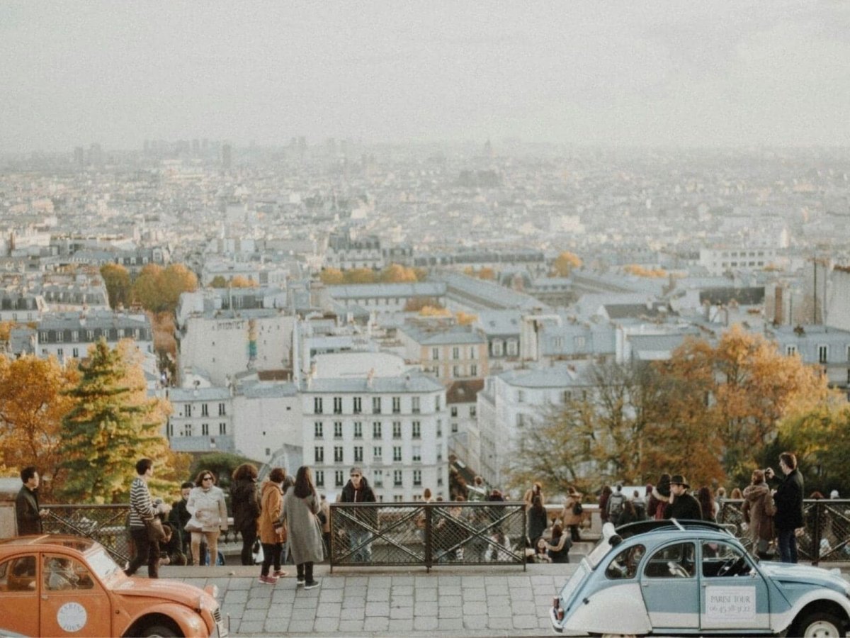 Menschen stehen an einer Aussichtsterrasse und blicken über eine weitläufige Stadtlandschaft im warmen Licht